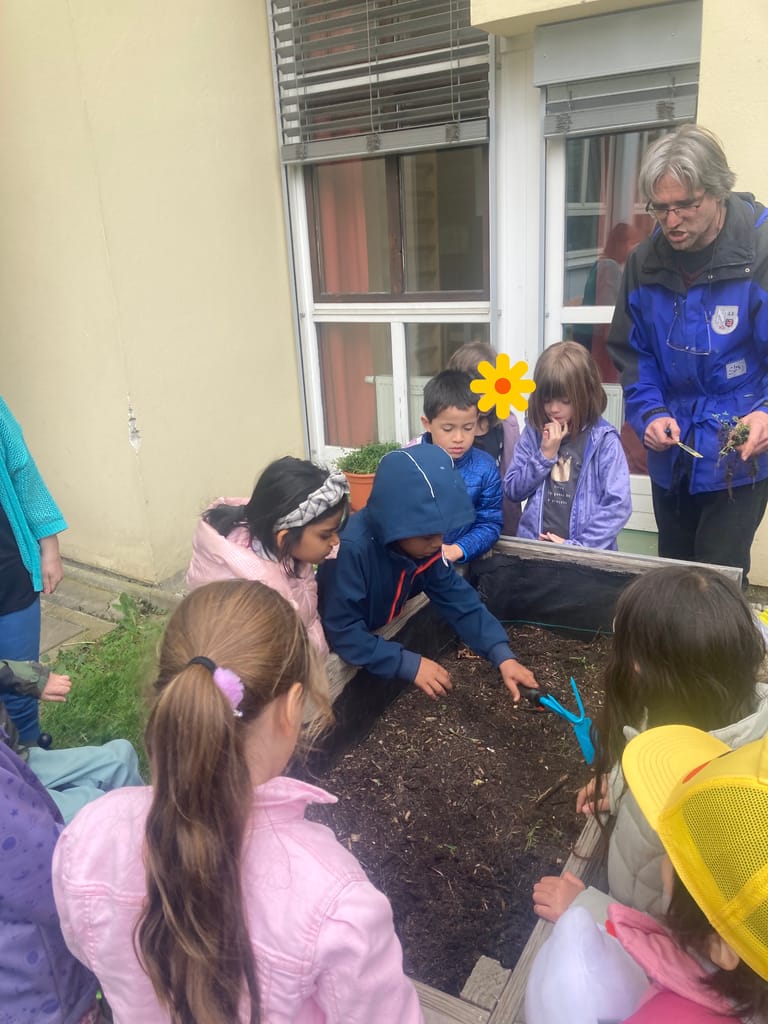 Kind lockert mit einer Hacke die Erde in einem Hochbeet