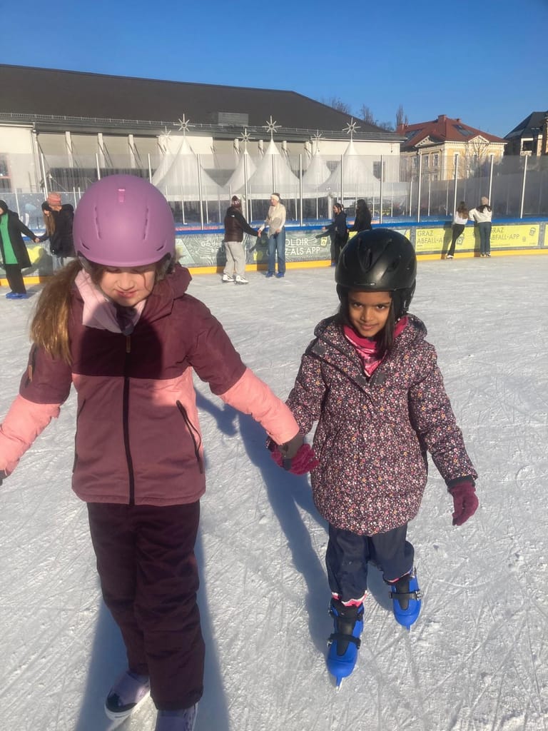 2 Kinder fahren Hand in Hand auf dem Eislaufplatz.