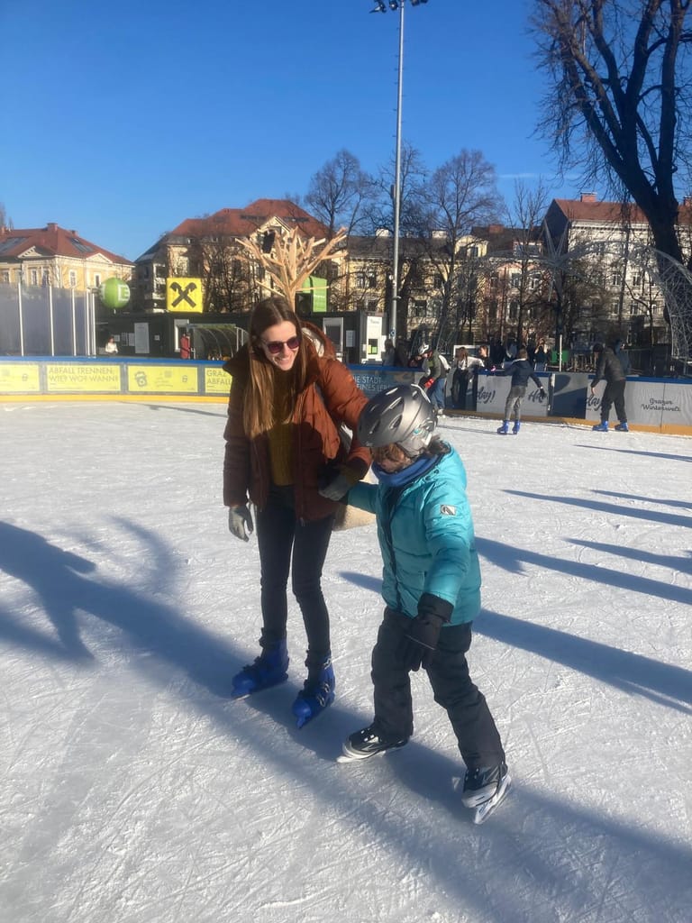 Lehrerin nimmt Kind am Eislaufplatz an die Hand.