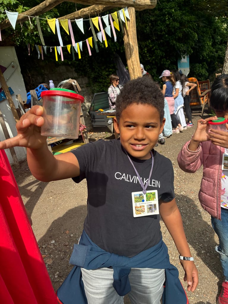 Kind hat ein Insekt in der Becherlupe gefangen.