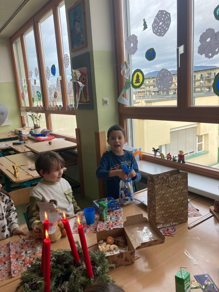 Kinder öffnen Wichtelgeschenke vor Adventkranz.