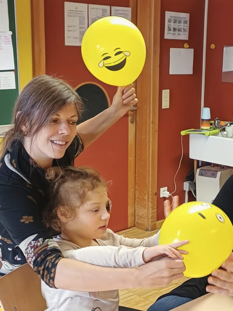 Kind spielt mit Luftballon, der eine Emotion abbildet.