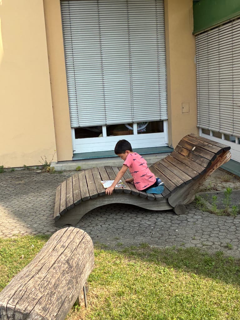 Kind liest auf einer Liegebank im Hof.