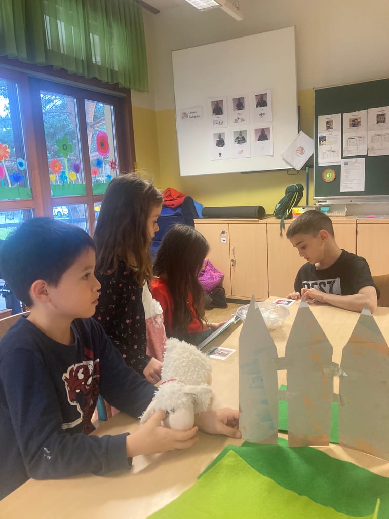 Kinder hüpfen mit Schafstofftier über eine gebastelte Wiese.