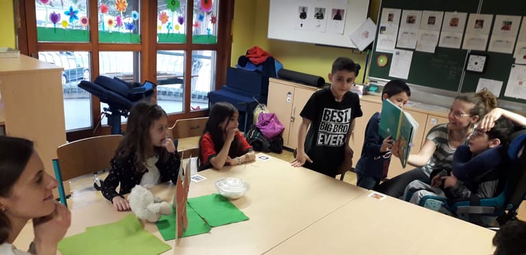 Kinder lesen einem Bub im Rollstuhl eine Geschichte vor.