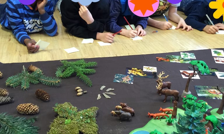 Kinder liegen vor Zapfen, Moos und Waldtierfiguren