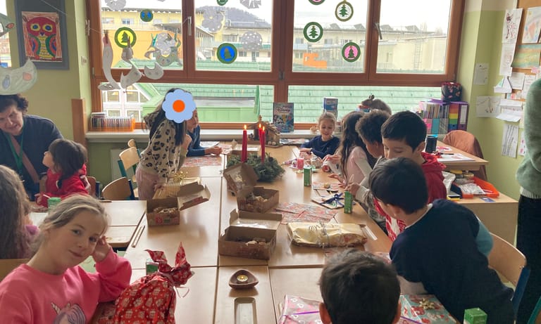 Kinder sitzen um großen Tisch mit Geschenken und Adventkranz