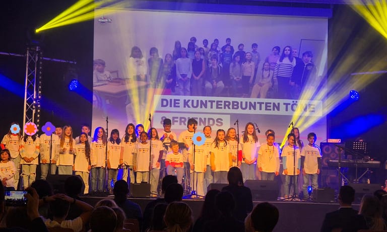 Kinder stehen auf einer Bühne und singen ein Lied.