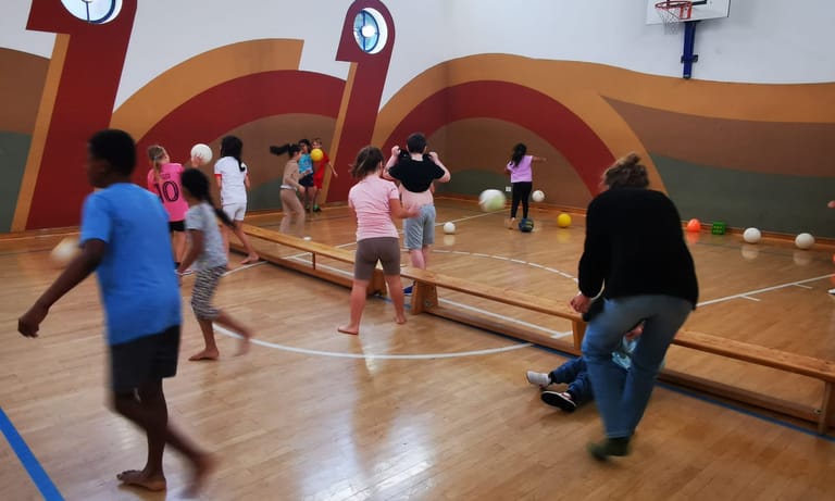 Kinder laufen durch den Turnsaal und werfen Bälle