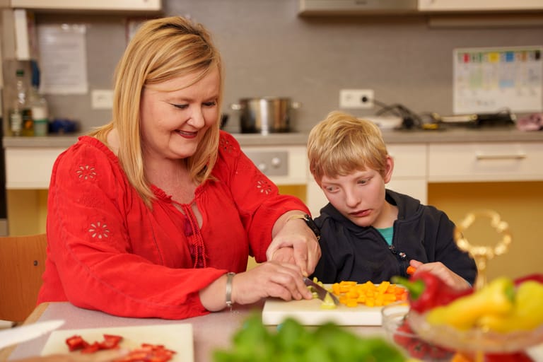 Frau schneidet mit Kind gemeinsam Gemüse.