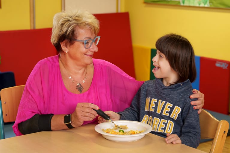 Frau sitzt mit Bub am Tisch und hat Gabel in der Hand.
