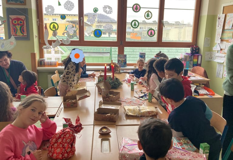 Kinder sitzen um großen Tisch mit Geschenken und Adventkranz