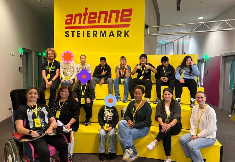 Klasse sitzt vor Antenne Steiermark Schild.