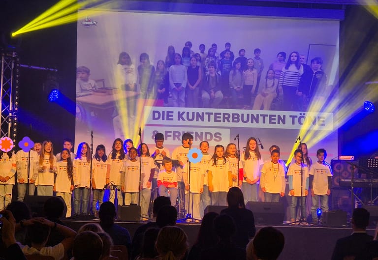 Kinder stehen auf einer Bühne und singen ein Lied.