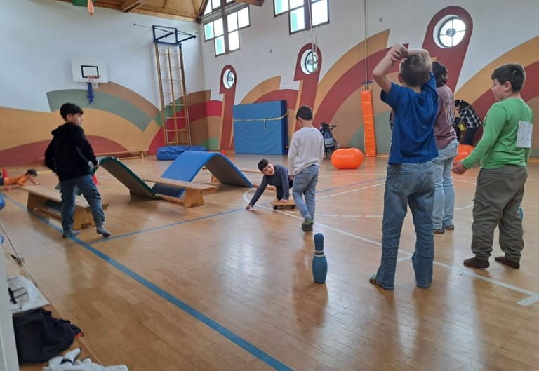 Kinder spielen im Turnsaal kegeln.