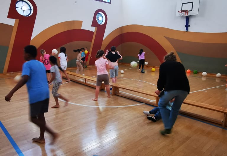 Kinder laufen durch den Turnsaal und werfen Bälle