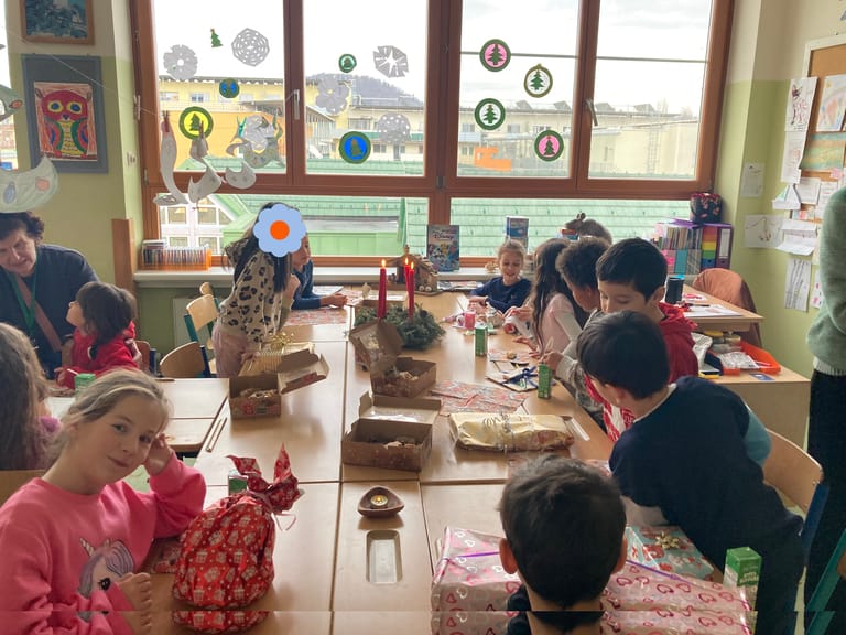 Kinder sitzen um großen Tisch mit Geschenken und Adventkranz