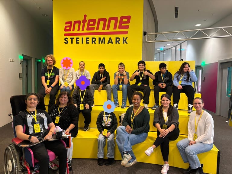 Klasse sitzt vor Antenne Steiermark Schild.