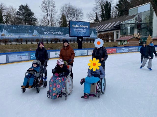 3 Begleitpersonen stehen mit Rollstühlen auf dem Eis.