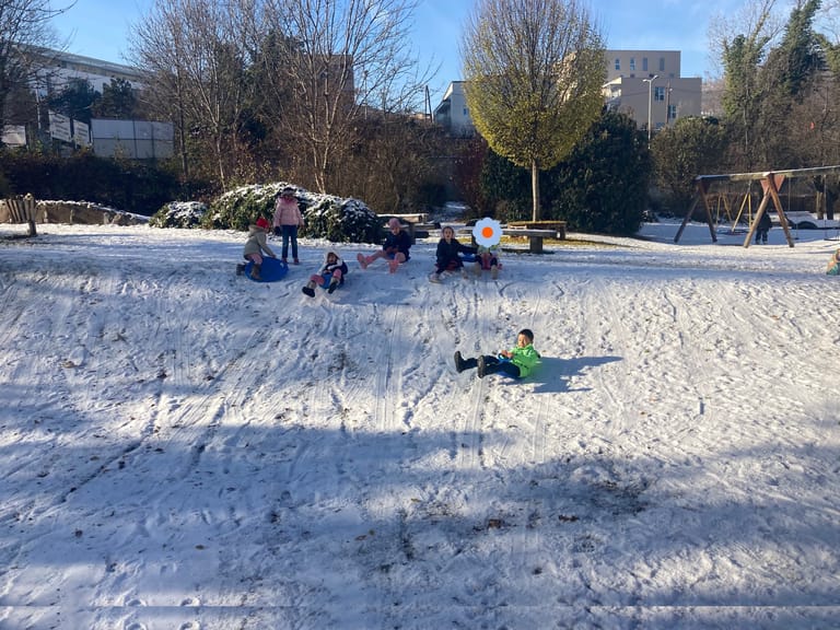 Kinder fahren mit Rodel den verschneiten Hügel hinab.