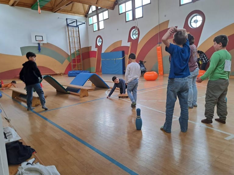 Kinder spielen im Turnsaal kegeln.