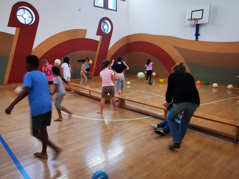 Kinder laufen durch den Turnsaal und werfen Bälle