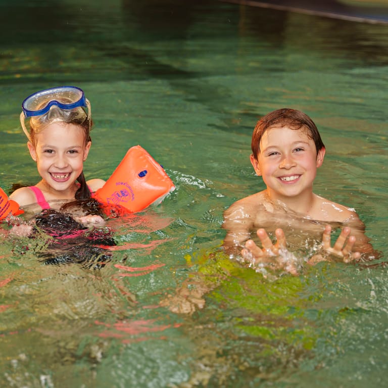 Zwei badende Kinder schwimmen und lächeln in die Kamera