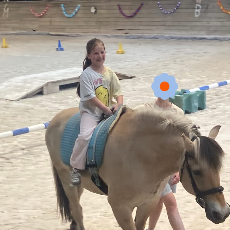 Kind sitzt auf einem Pferd und lächelt.