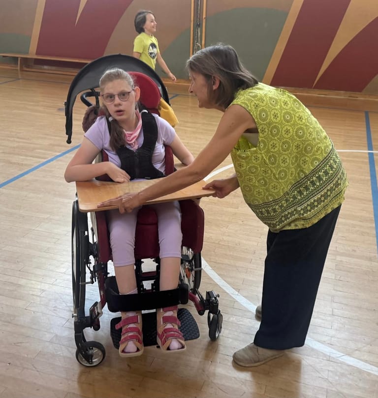 Lehrerin betreut Kind im Rollstuhl im Turnsaal.