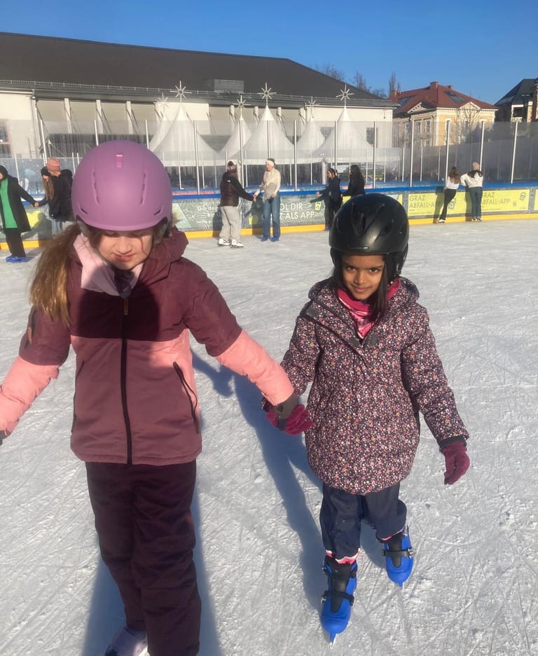 2 Kinder fahren Hand in Hand auf dem Eislaufplatz.