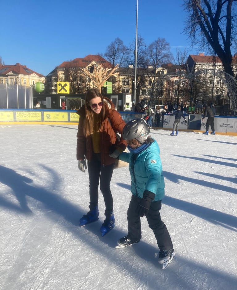 Lehrerin nimmt Kind am Eislaufplatz an die Hand.