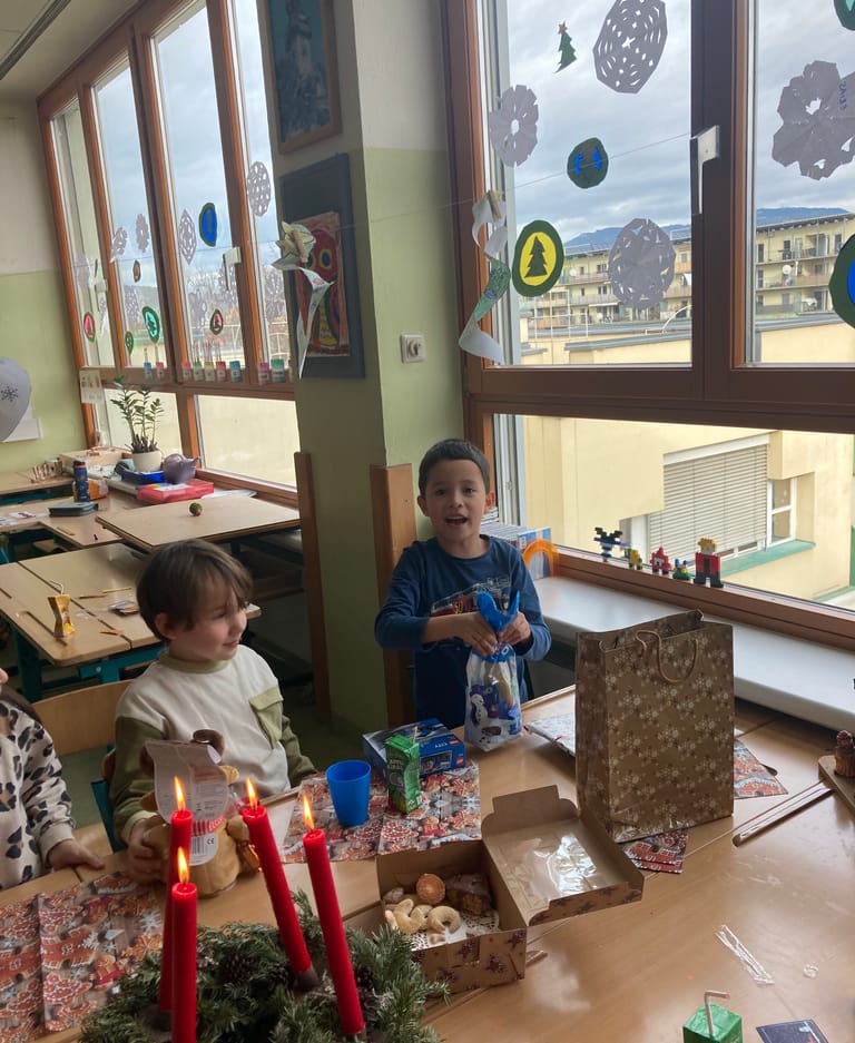 Kinder öffnen Wichtelgeschenke vor Adventkranz.