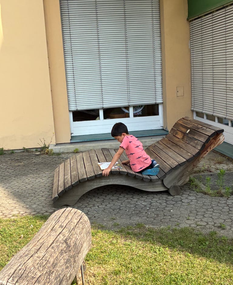 Kind liest auf einer Liegebank im Hof.
