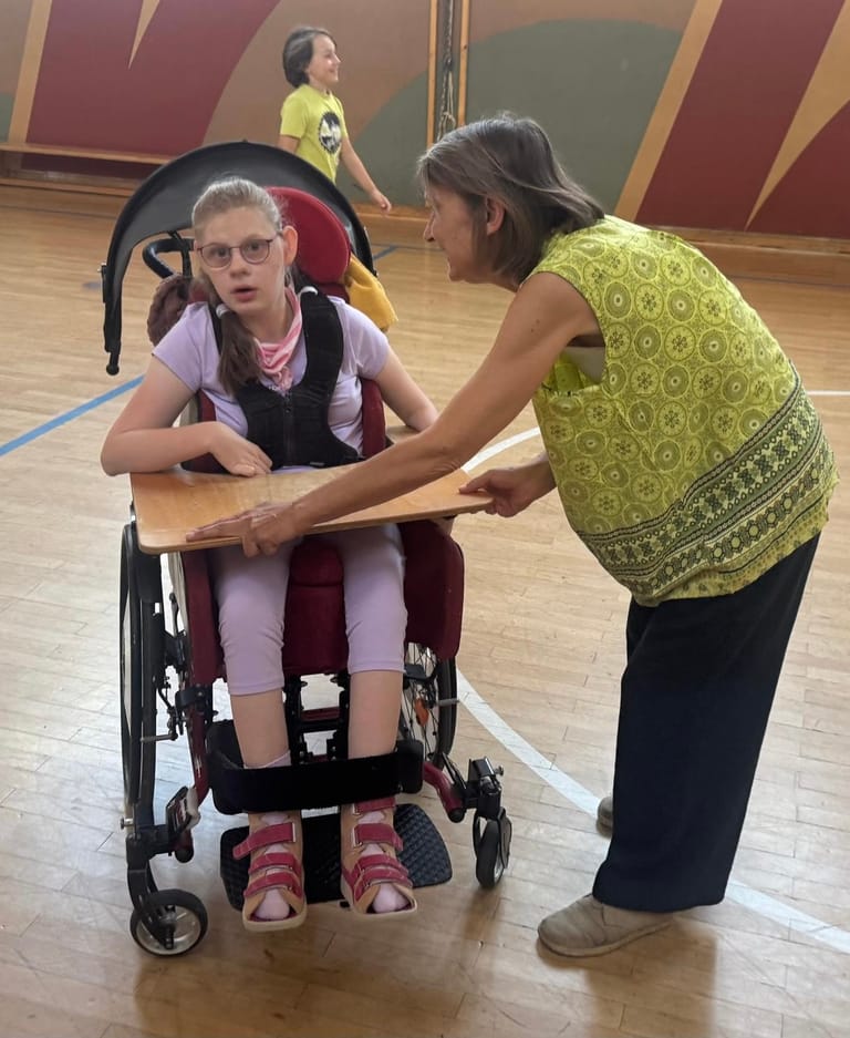 Lehrerin betreut Kind im Rollstuhl im Turnsaal.