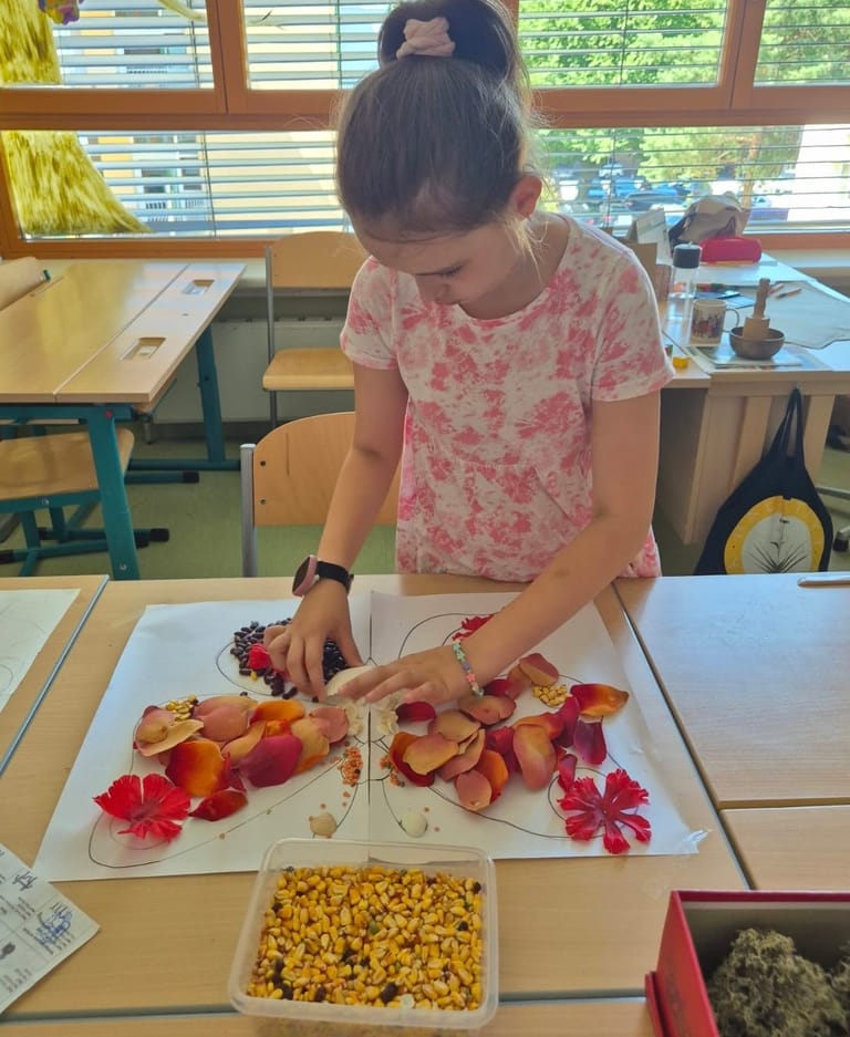 Mädchen legt mit Blüten Figur auf Zettel nach.